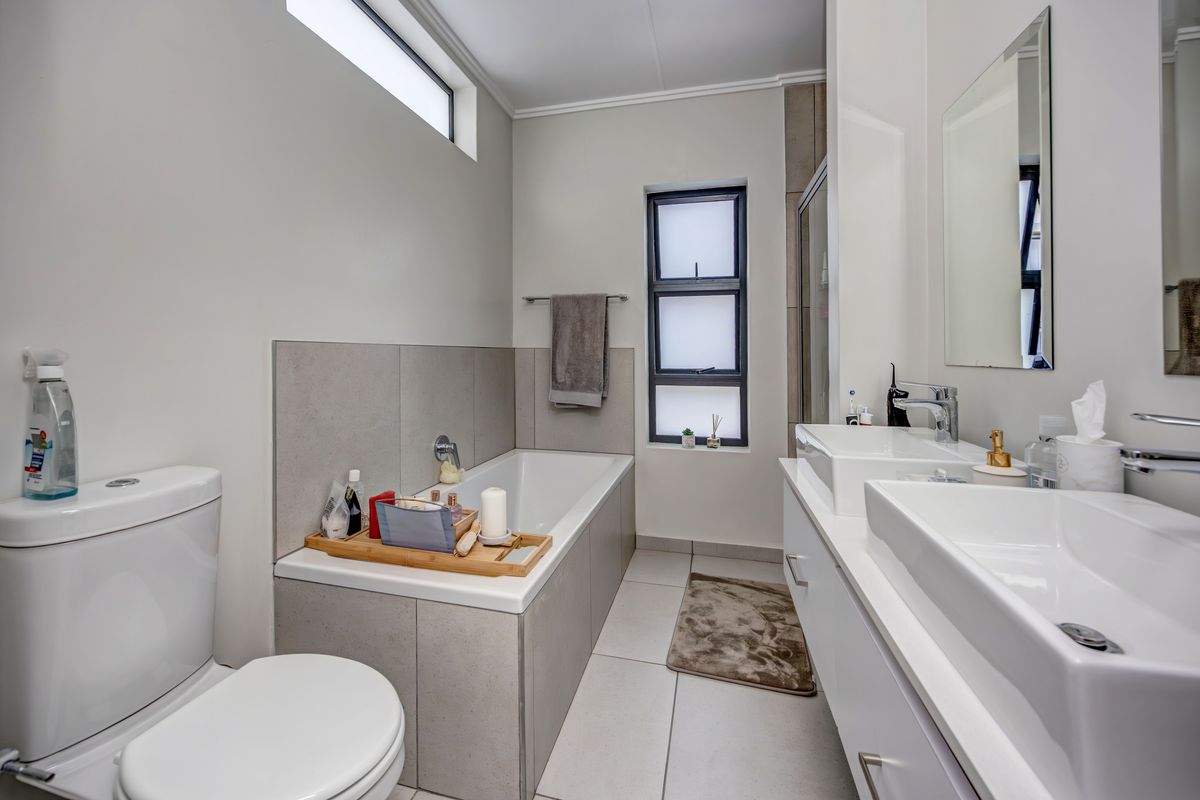 Modern bathroom featuring a double vanity with integrated basins, a tiled bathtub, and a separate shower enclosure with neutral finishes.