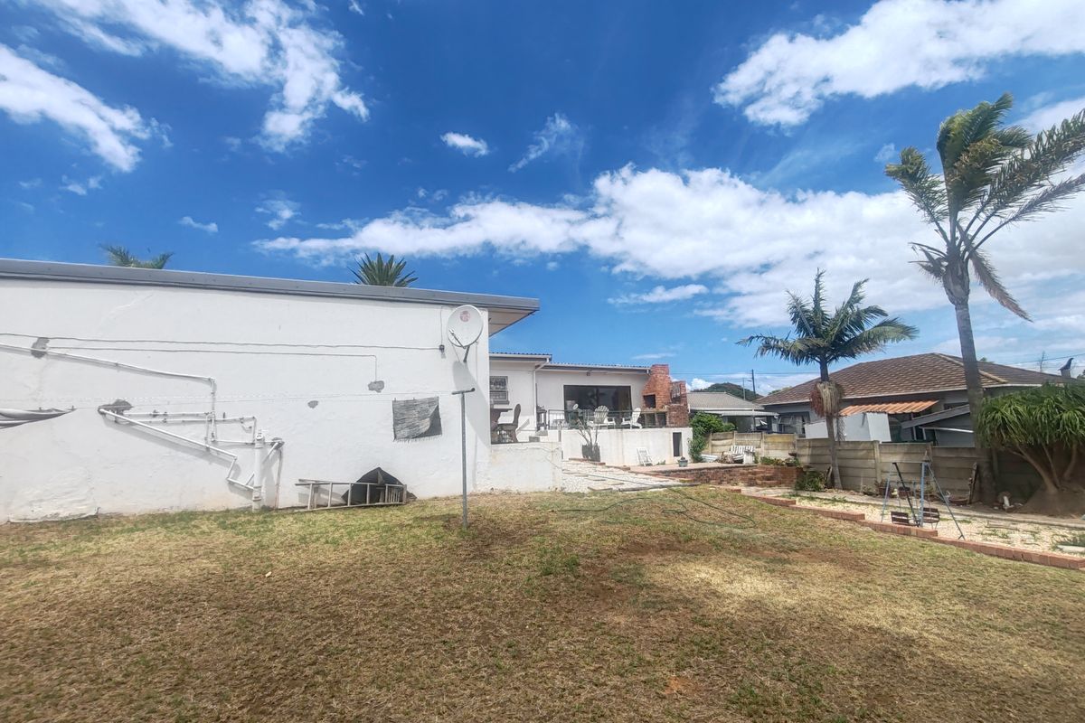 Rear view of the property featuring a lawn, concrete patio area, and an outdoor brick fireplace.