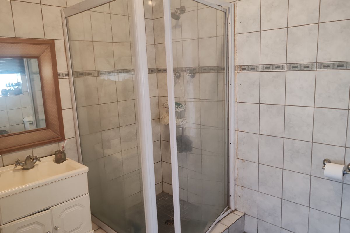 A functional bathroom featuring a corner shower enclosure, vanity basin, and tiled wall finishes, currently showing signs of wear and dated fixtures.