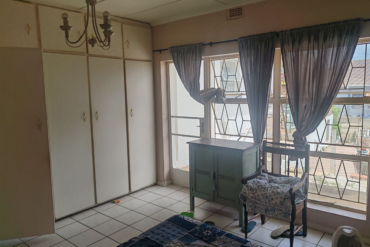 A bedroom featuring built-in cupboards, tiled flooring, and large windows with security bars, offering a functional space in need of cosmetic updates.