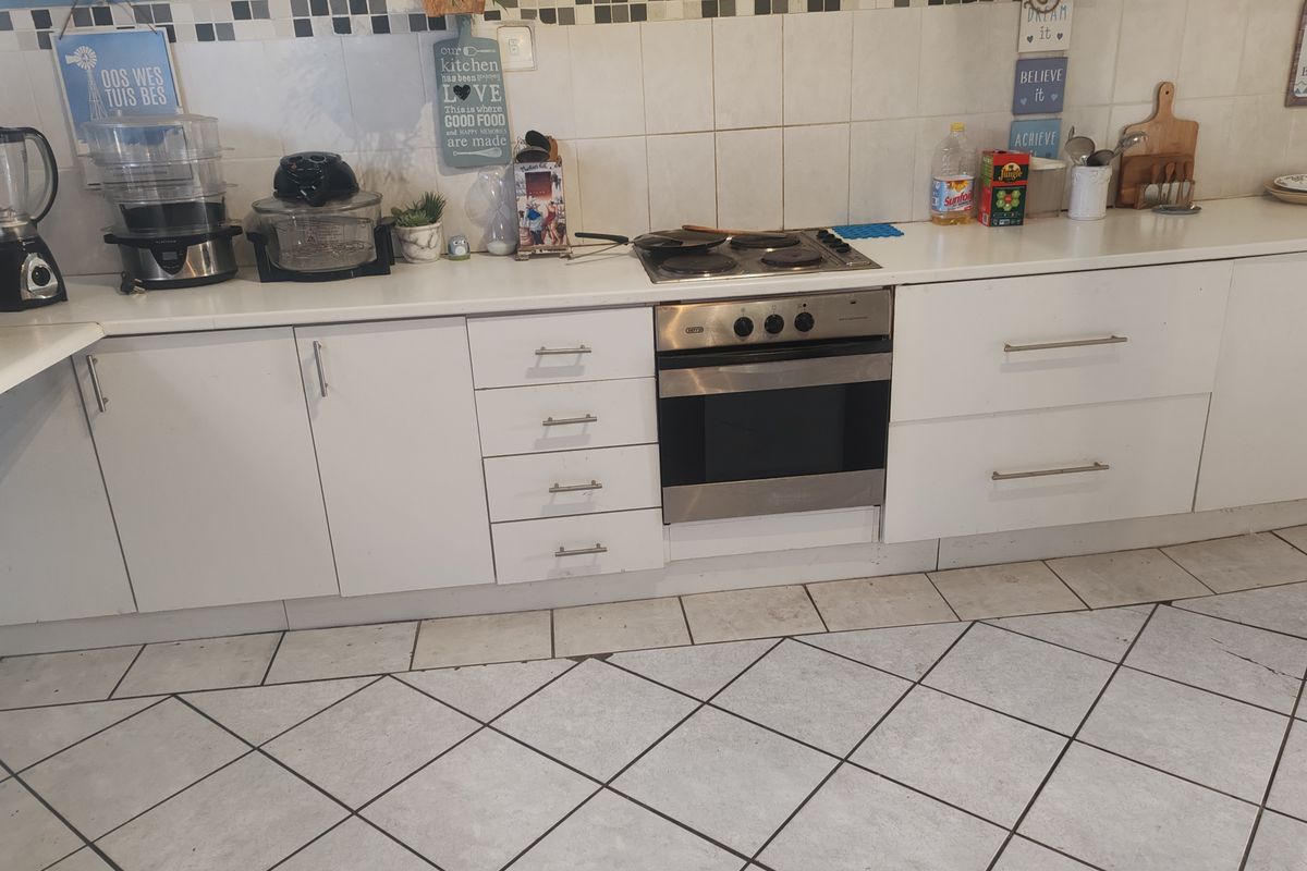 A functional kitchen featuring white cabinetry, a built-in oven with electric hob, stone countertops, and a tiled splashback with ceramic floor tiles.