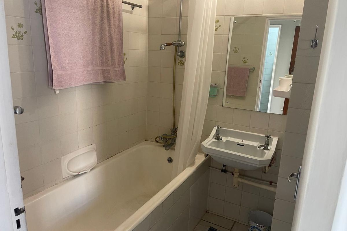 A compact, dated bathroom featuring a standard bathtub with shower mixer, wall-mounted basin, and tiled surfaces throughout.