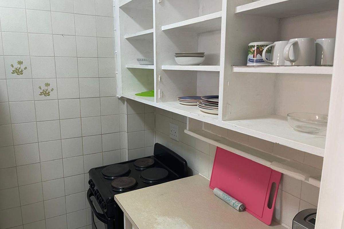 A compact kitchen area featuring built-in open shelving, tiled walls, and a freestanding electric stove with a laminate countertop.
