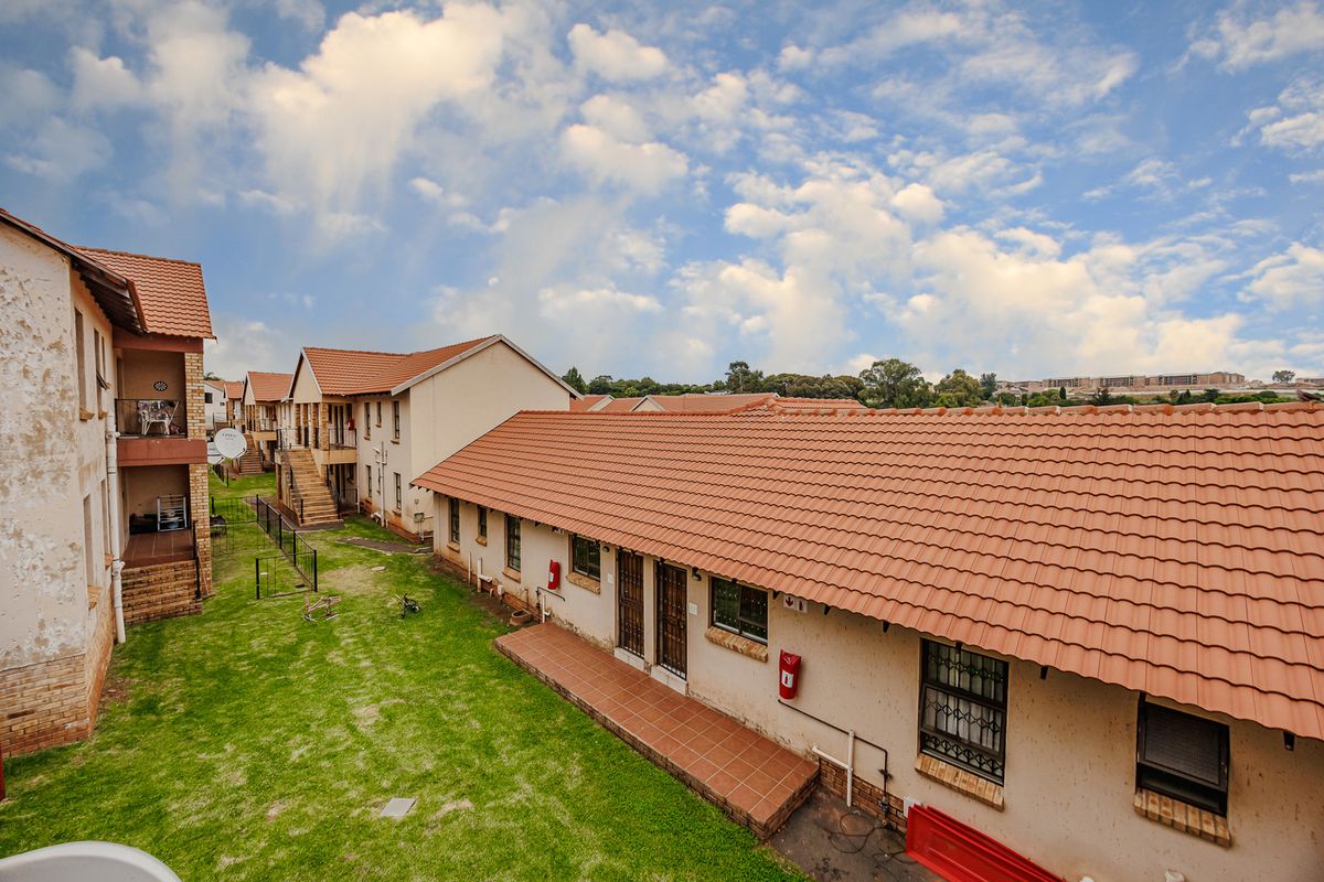 An elevated view of the townhouse complex rear exterior, featuring tiled roofing, communal lawn space, and paved patio areas.