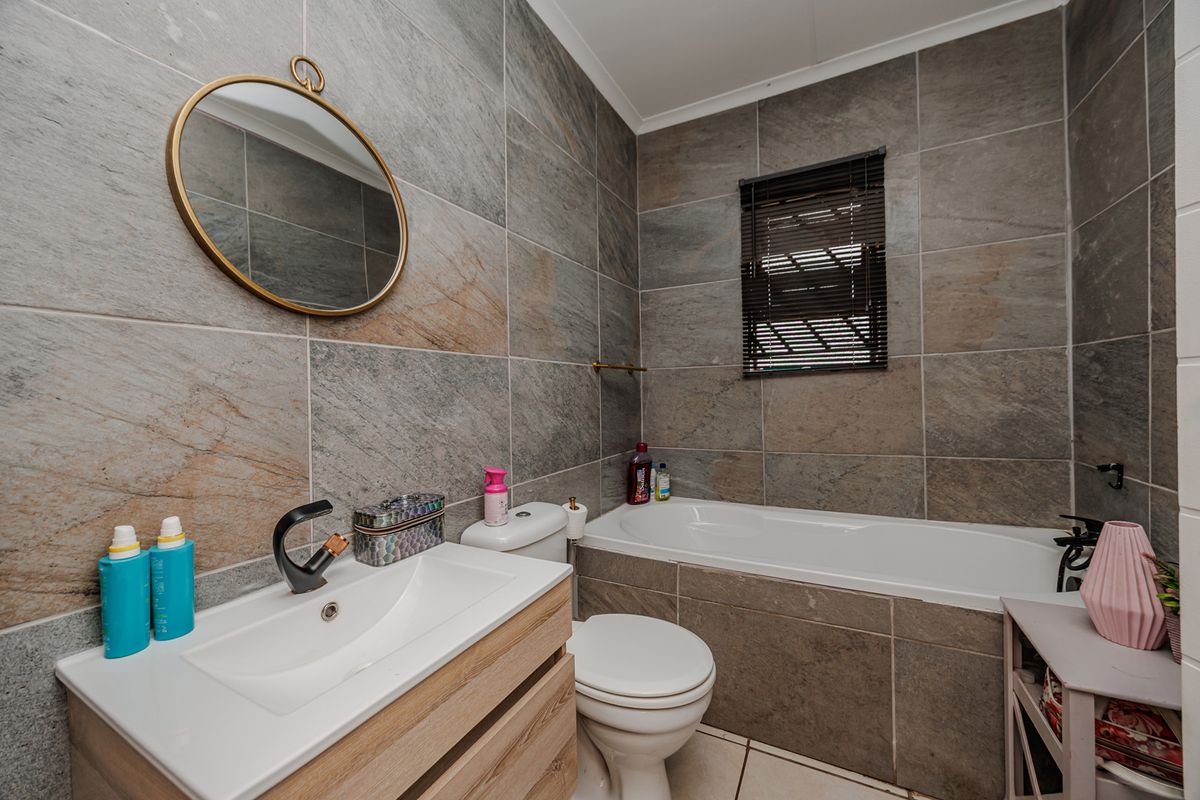 Modern bathroom featuring large-format stone-look wall tiles, a vanity with integrated basin, a bathtub, and a toilet.