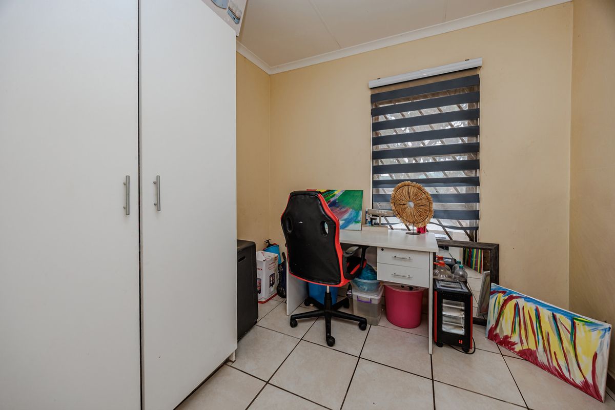 A functional bedroom featuring tiled flooring, a built-in wardrobe, and a window fitted with a modern roller blind.
