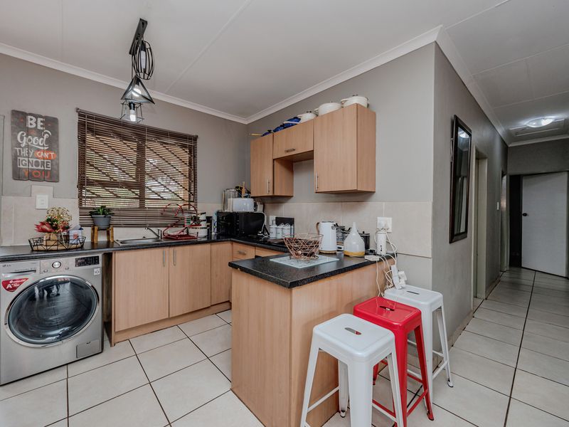 Compact kitchen featuring light wood cabinetry, dark laminate countertops, tiled flooring, and integrated laundry plumbing, offering a functional layout for a townhouse.