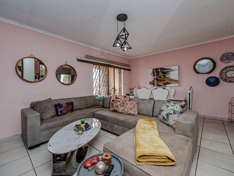 Open-plan living and dining area featuring ceramic floor tiles, a modern geometric pendant light, and access to an outdoor space via a security gate.