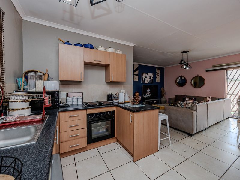 Open-plan kitchen and living area featuring built-in cabinetry, tiled flooring, and direct access to an outdoor space through a security gate.