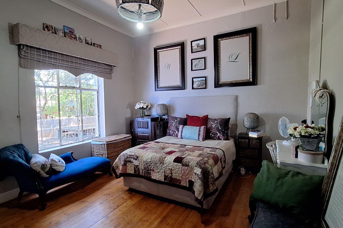 A well-maintained bedroom featuring original polished timber flooring, large window with pelmet, and a decorative ceiling light fixture.