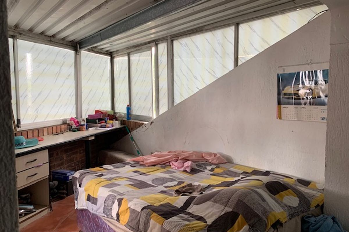 A bedroom featuring a sloped ceiling, built-in desk area, and tiled flooring, offering potential for modernization and improved interior finishes.