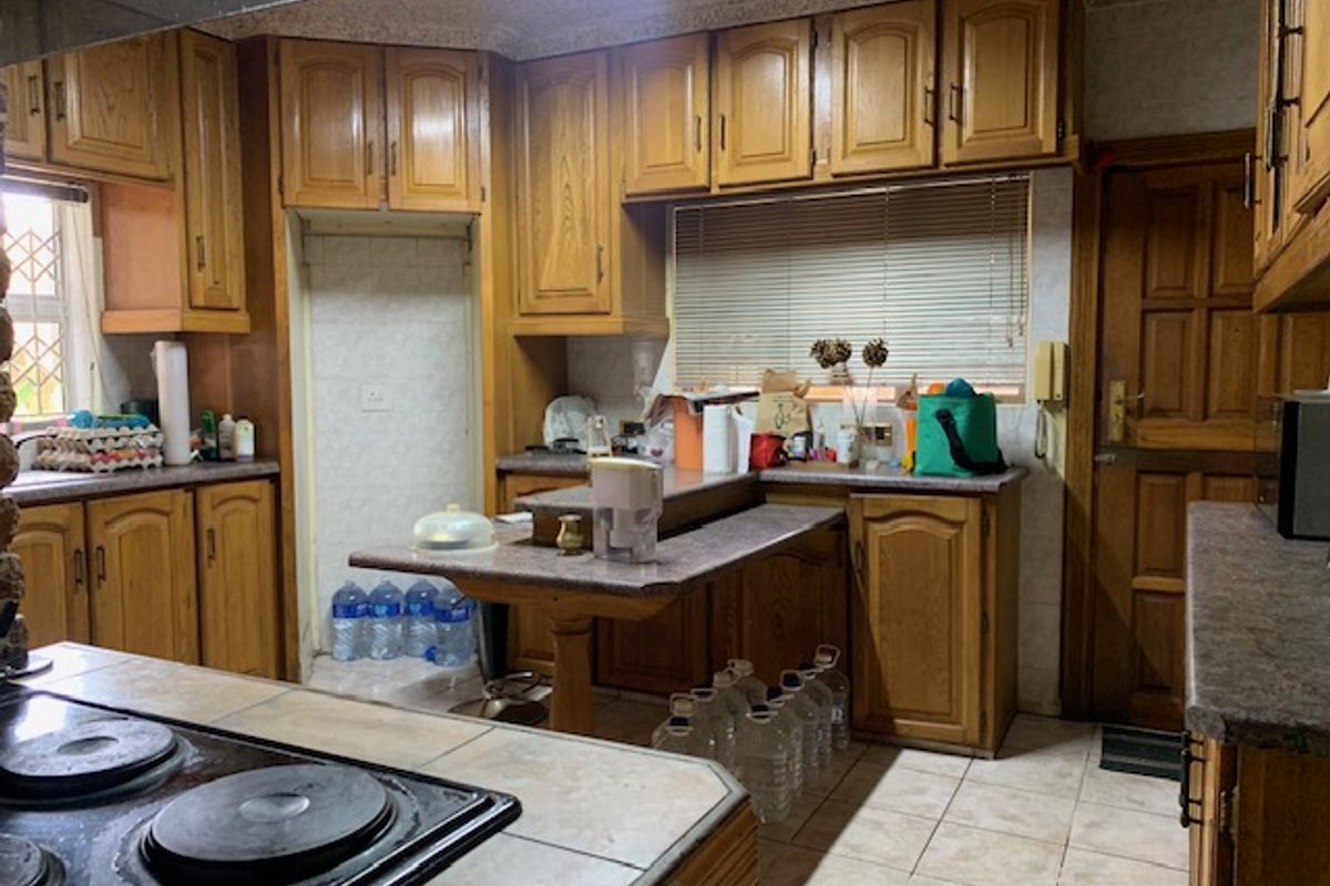 A dated kitchen featuring traditional wooden cabinetry, laminate countertops, and an integrated electric hob with an overhead extractor fan.