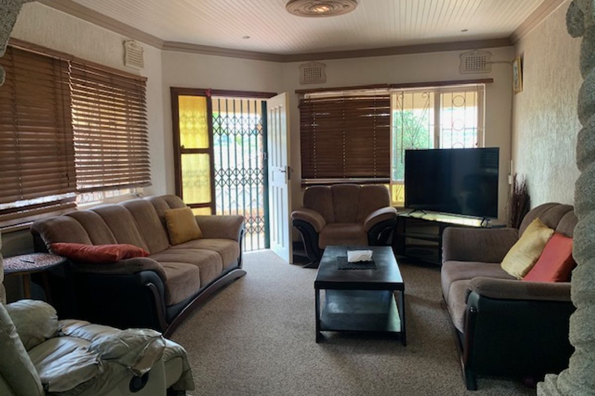 A comfortable living room featuring a beadboard ceiling with a decorative rose, security gate access, and venetian blinds on the windows.
