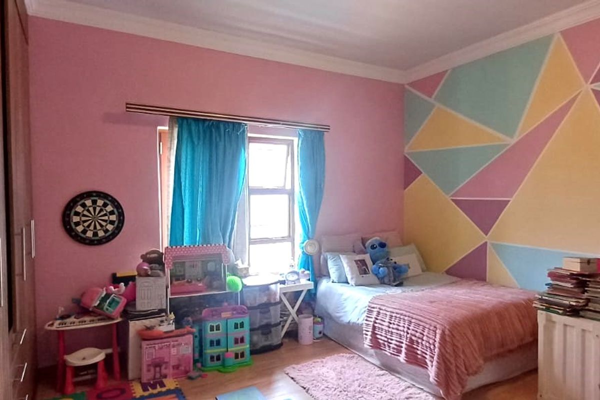 A bedroom featuring laminate flooring, built-in wardrobes, and decorative wall paint, offering a functional space with potential for updated styling.