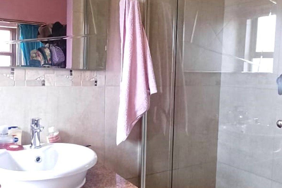 A functional bathroom featuring a vanity cabinet with a vessel sink, granite-style countertop, and a glass-enclosed shower with tiled walls.