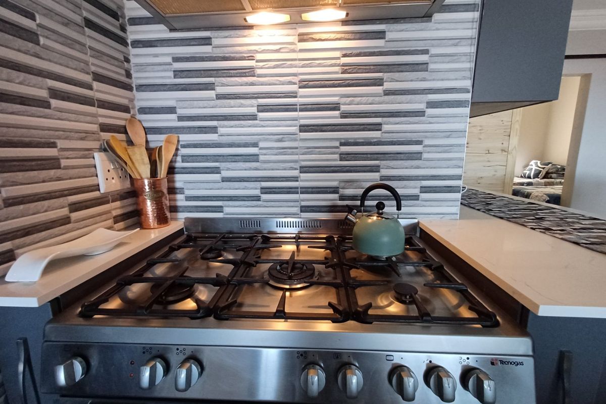 A close-up view of a kitchen cooktop area featuring a stainless steel gas stove, extractor fan, and modern textured tiled splashback.