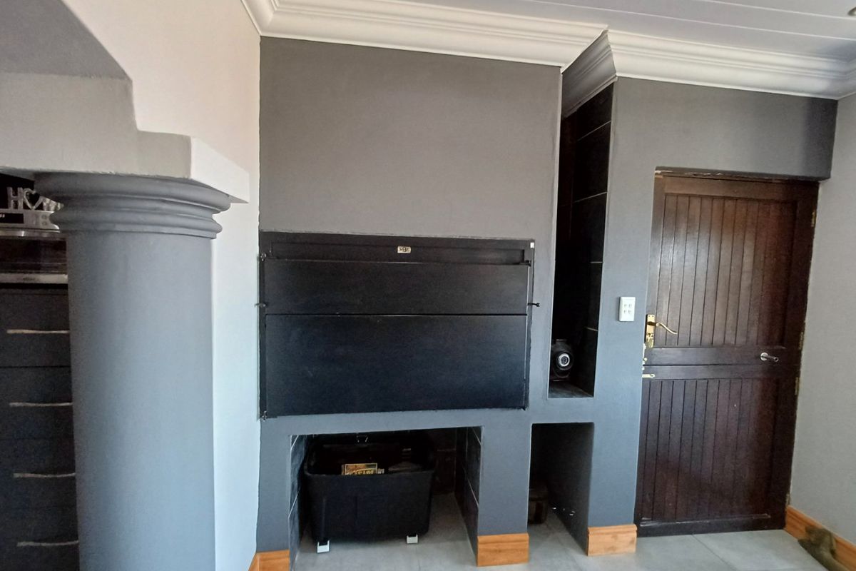 Indoor built-in braai area featuring a dark grey finish, decorative column, and wooden door access, set within a tiled living space.