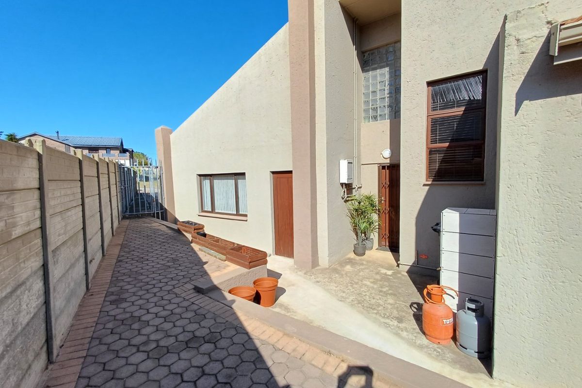 A side exterior view of the property featuring paved walkways, a security gate, and a concrete boundary wall.