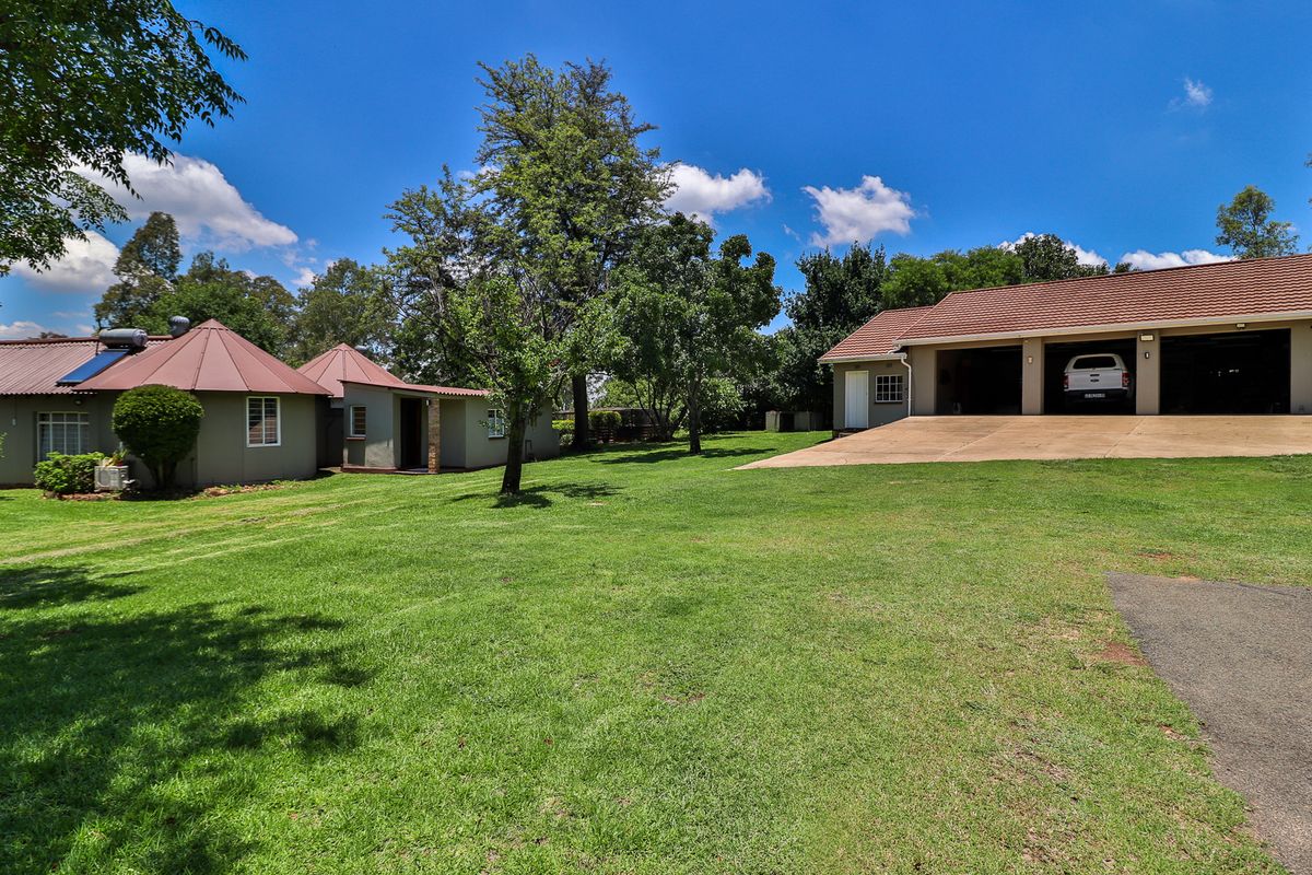 Spacious rear garden area featuring a triple garage, well-maintained lawn, and a dwelling with a solar geyser system.