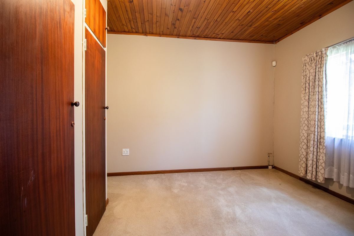 A vacant bedroom featuring built-in wooden cupboards, a classic timber-paneled ceiling, and neutral carpeting.