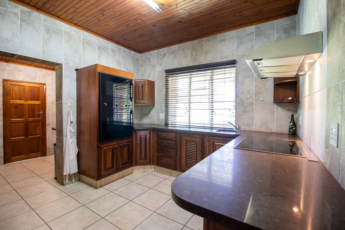 A functional kitchen featuring wooden cabinetry, stone countertops, built-in oven, electric hob, and tiled finishes with a warm wooden ceiling.