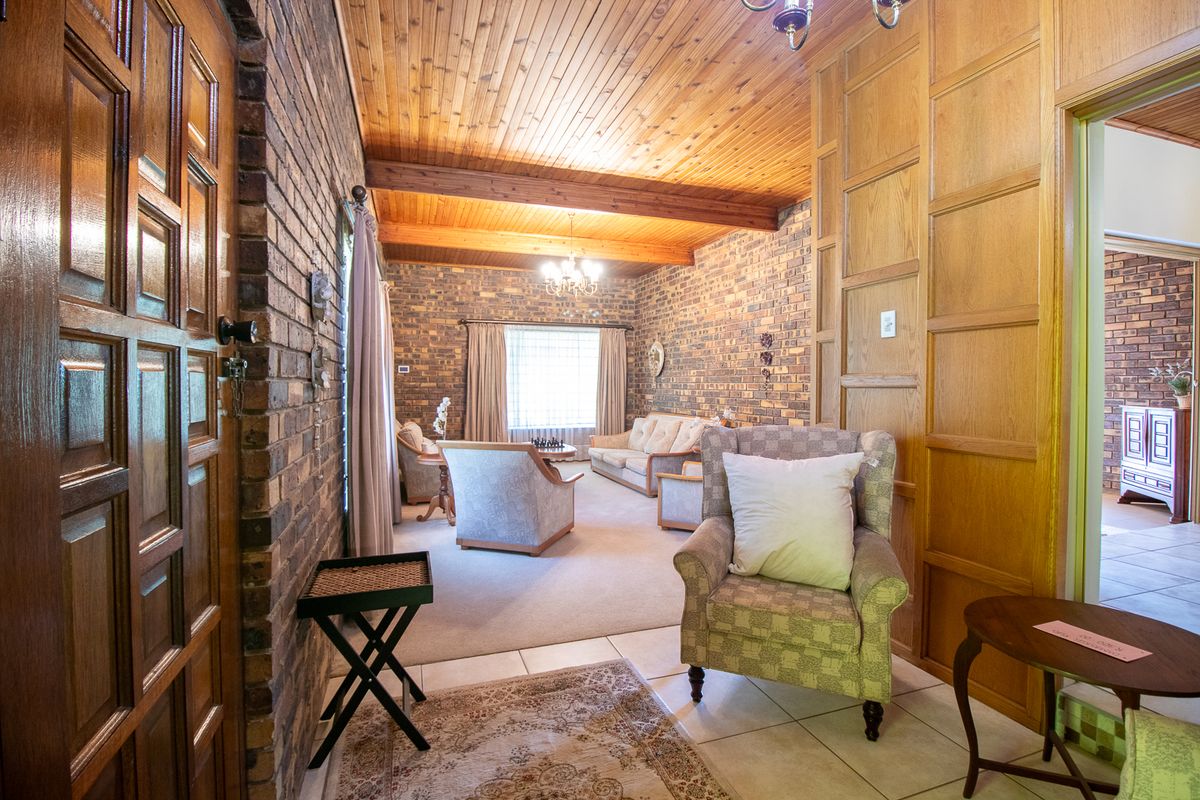 A spacious living area featuring exposed brick walls, timber ceiling beams, and a combination of tiled and carpeted flooring with warm lighting.