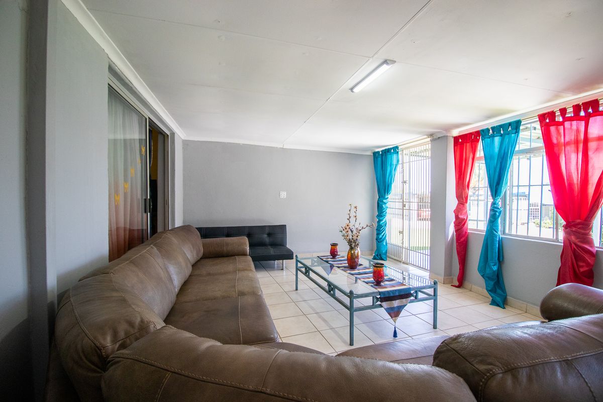A spacious living area featuring tiled flooring, a sliding glass door, and a security gate, providing a functional and well-lit space.