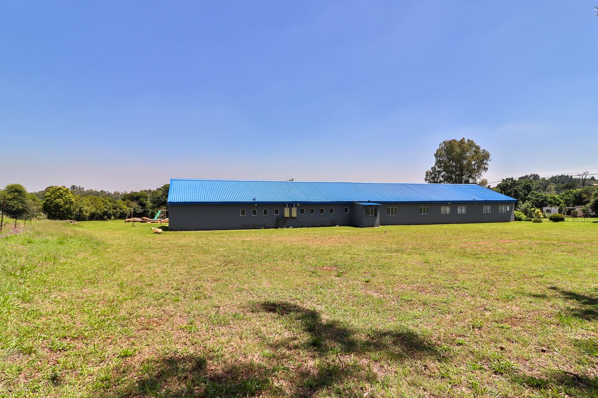 A wide-angle view of the rear exterior of a large outbuilding featuring a blue corrugated metal roof set on a spacious grassy plot.