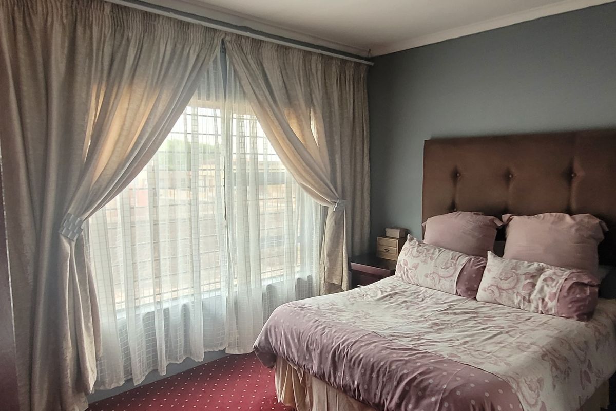 A bedroom featuring carpeted flooring and a large window fitted with security bars, providing natural light.