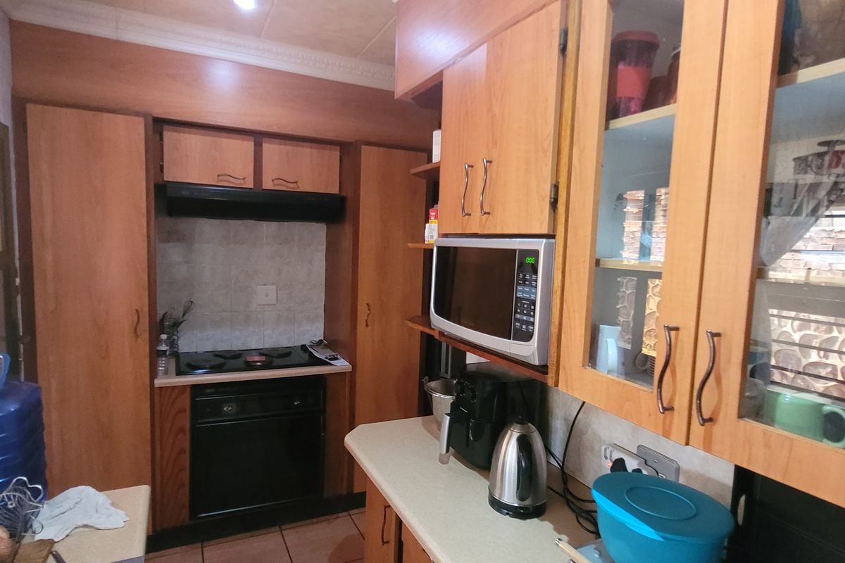 A functional kitchen featuring wooden cabinetry, laminate countertops, a built-in oven with gas hob, and tiled flooring.
