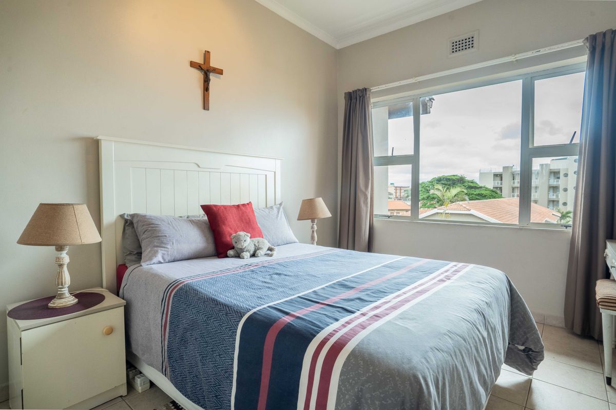 A well-lit bedroom featuring tiled flooring, a large window with exterior views, and neutral wall finishes.