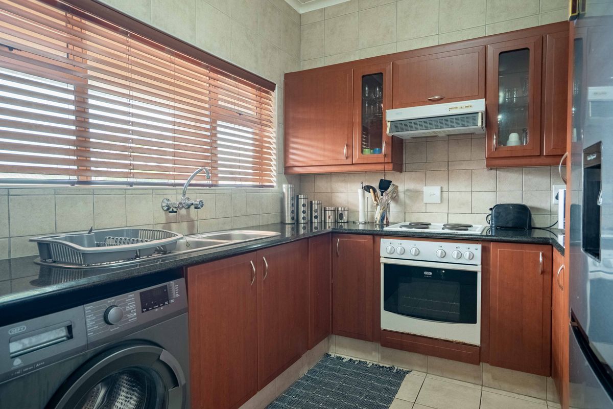 A functional kitchen featuring wooden cabinetry, granite countertops, a double sink, and built-in electric stove with extractor fan.