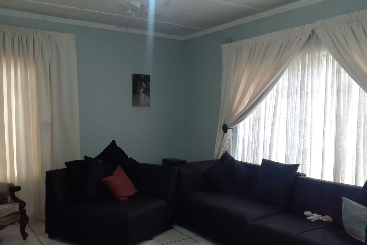 A living room featuring tiled flooring and large windows with curtains, providing natural light to the space.