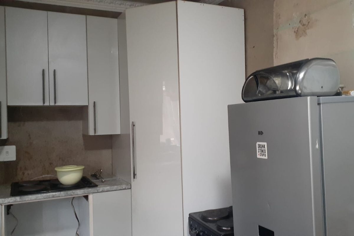 A kitchen area featuring white cabinetry, a built-in hob, and unfinished wall surfaces requiring repair and completion.