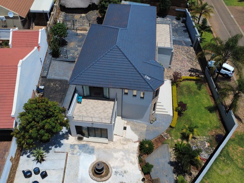 Aerial view of the property showcasing the tiled roof, paved driveway, landscaped garden, and rear balcony area.