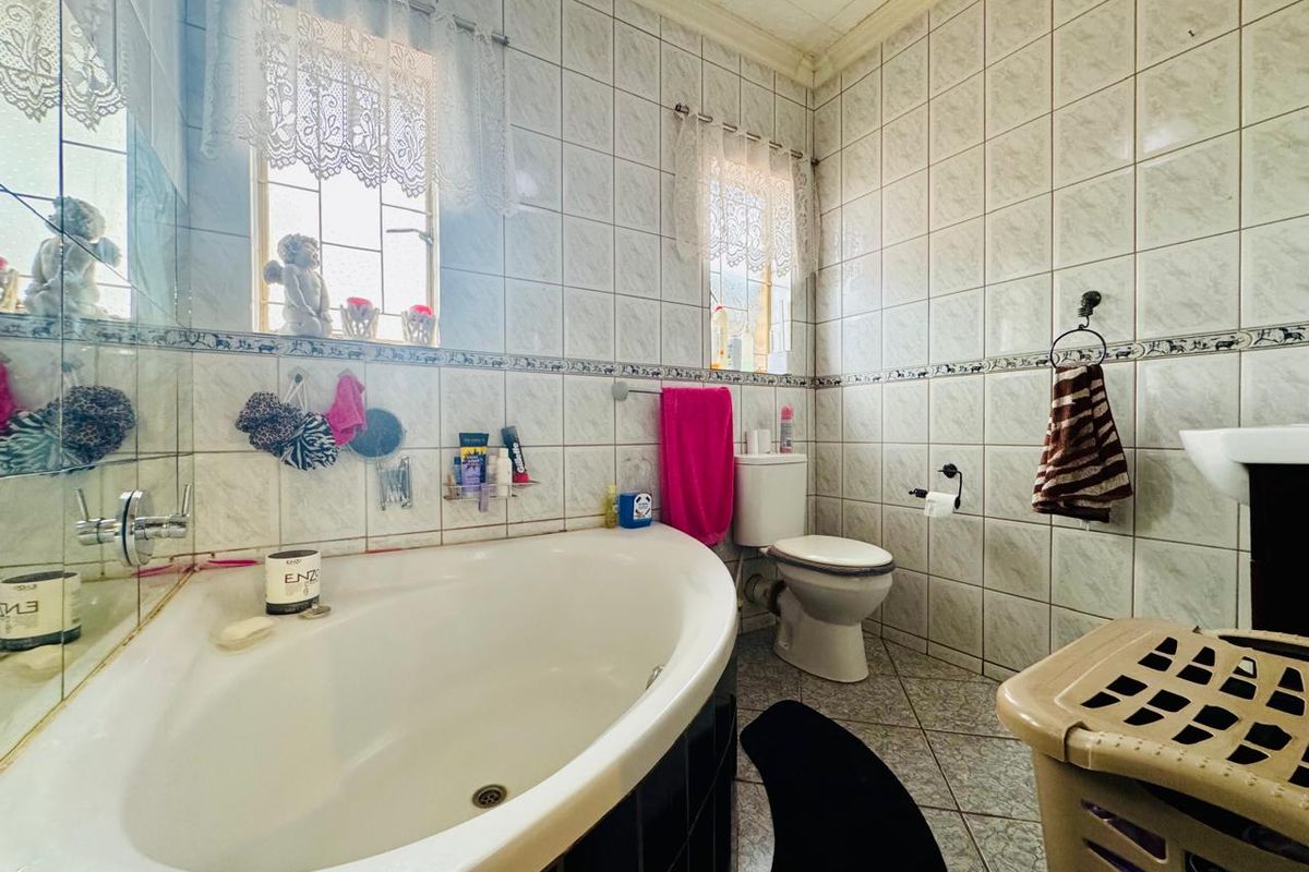 A dated bathroom featuring a corner bathtub, toilet, and full-height wall tiling with decorative border accents.