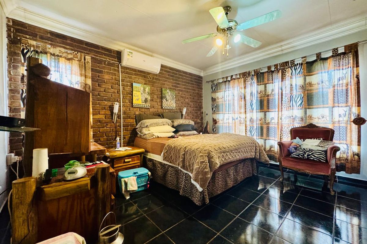Spacious bedroom featuring a rustic exposed brick feature wall, dark tiled flooring, ceiling fan, and wall-mounted air conditioning unit.