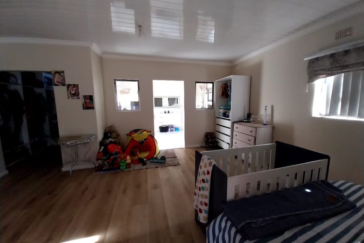 Spacious bedroom featuring laminate flooring, glossy ceiling panels, and built-in storage, offering a functional layout with natural light.