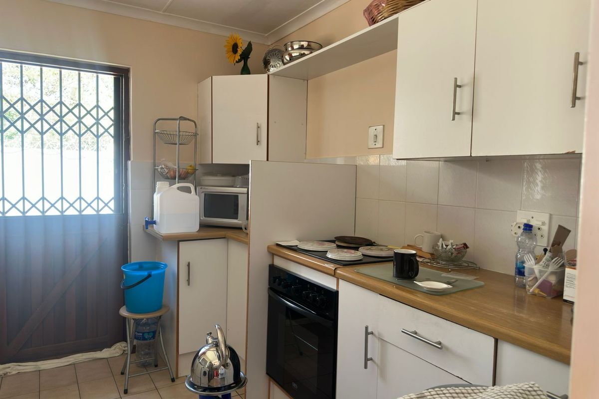 A functional kitchen featuring white cabinetry, laminate countertops, and a built-in electric oven and hob, with direct access to an exterior security door.