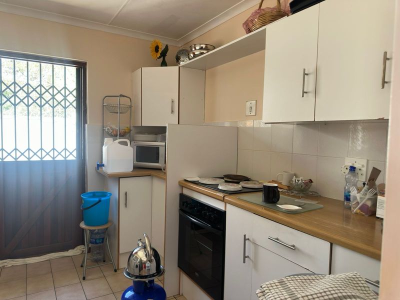A functional kitchen featuring white cabinetry, laminate countertops, and a built-in electric oven and hob, with direct access to an exterior security door.