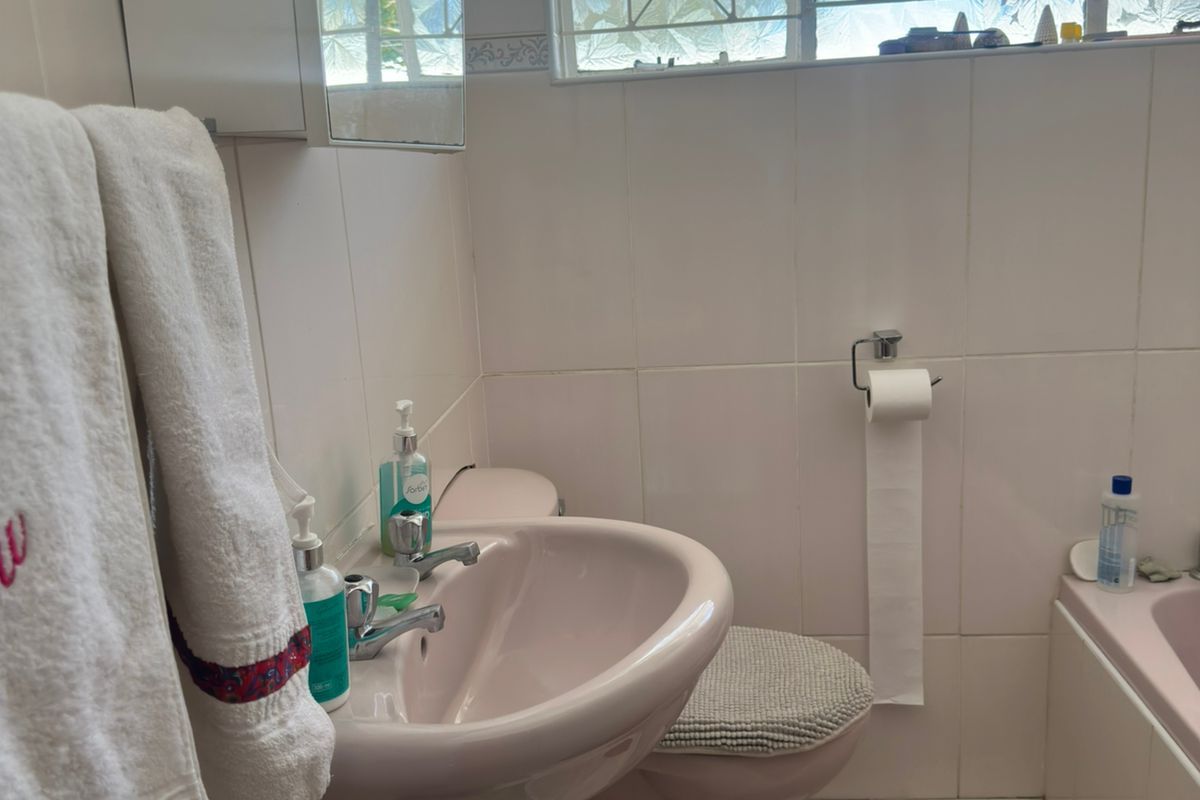 A functional bathroom featuring a pedestal basin, toilet, and bathtub with tiled finishes and a window with security bars.
