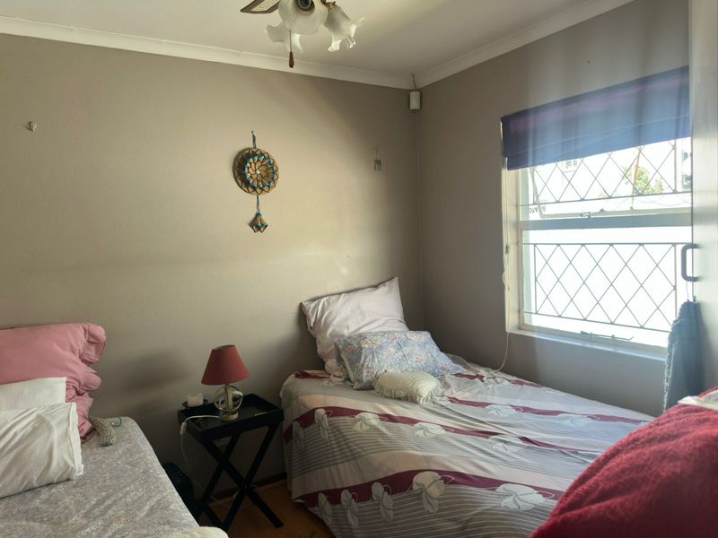 A functional bedroom featuring a leaded glass window, ceiling fan, and neutral wall finishes, offering a comfortable space for rest.