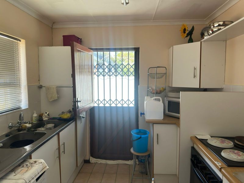 A functional kitchen featuring built-in cabinetry, a stainless steel sink, and a built-in oven, with direct access to the exterior via a security gate.
