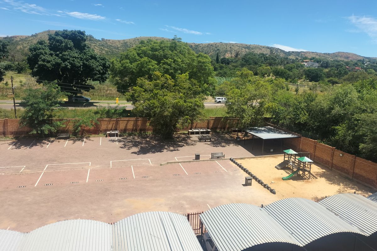Aerial view of the property grounds featuring a paved parking area, covered carports, a children's playground, and a brick boundary wall.