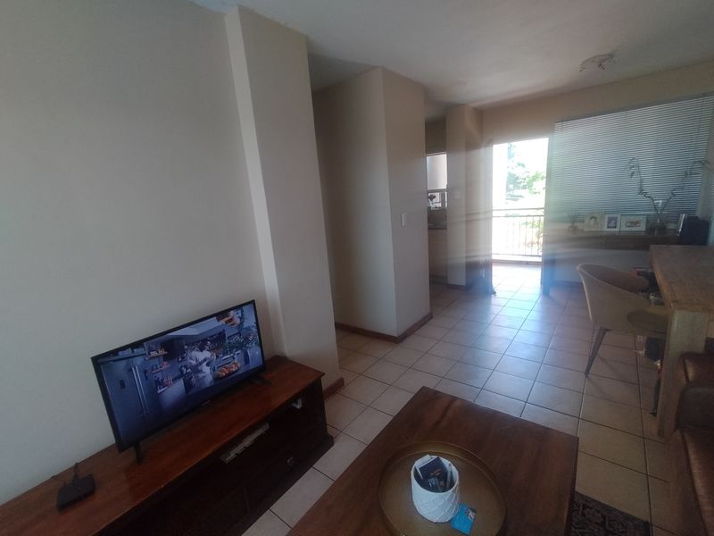 Open plan living area featuring tiled flooring and access to a balcony through a sliding door with venetian blinds.
