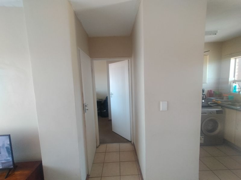A neutral-toned hallway connecting the living area to the bedroom and kitchen, featuring tiled flooring and standard internal doors.