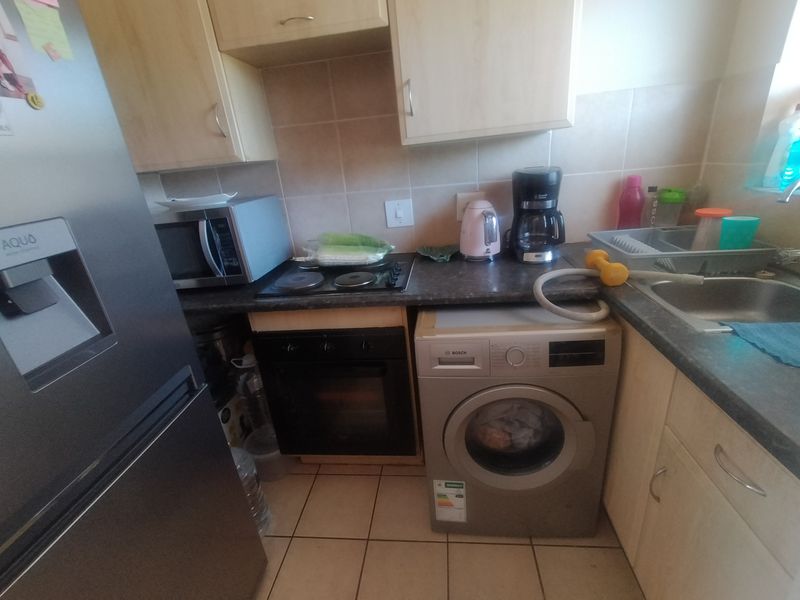 Compact kitchen featuring light wood-finish cabinetry, dark laminate countertops, built-in oven, electric hob, and an integrated washing machine with tiled splashback and flooring.