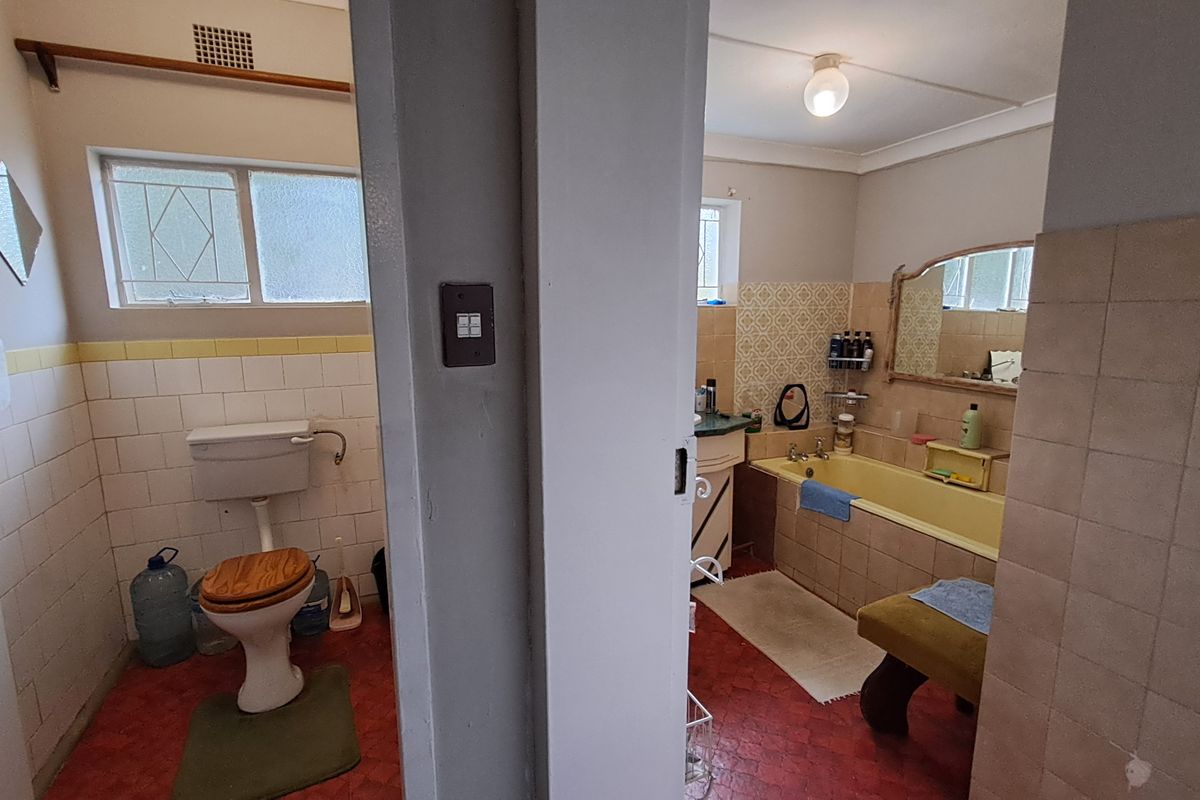 A dated bathroom featuring a built-in bathtub, toilet, and vanity basin with original wall and floor tiling, offering significant potential for modernization.