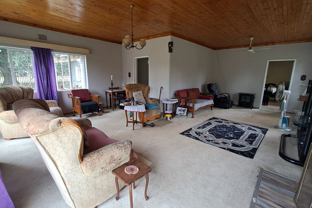 Spacious living room featuring a timber tongue and groove ceiling, fireplace, and large windows, offering a dated interior ready for modernization.