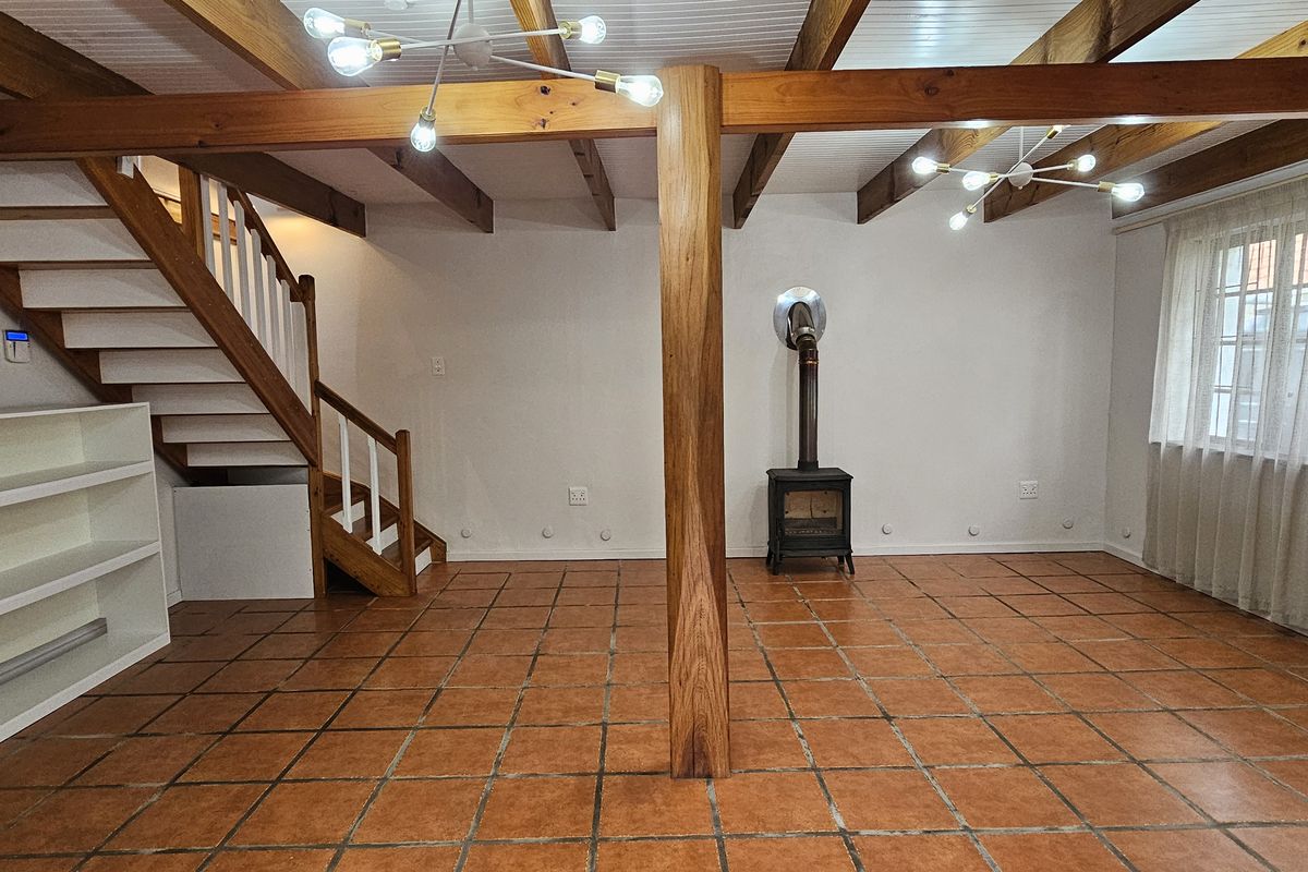 Spacious living area featuring exposed timber beams, terracotta floor tiles, a central timber support column, and a cast iron fireplace.